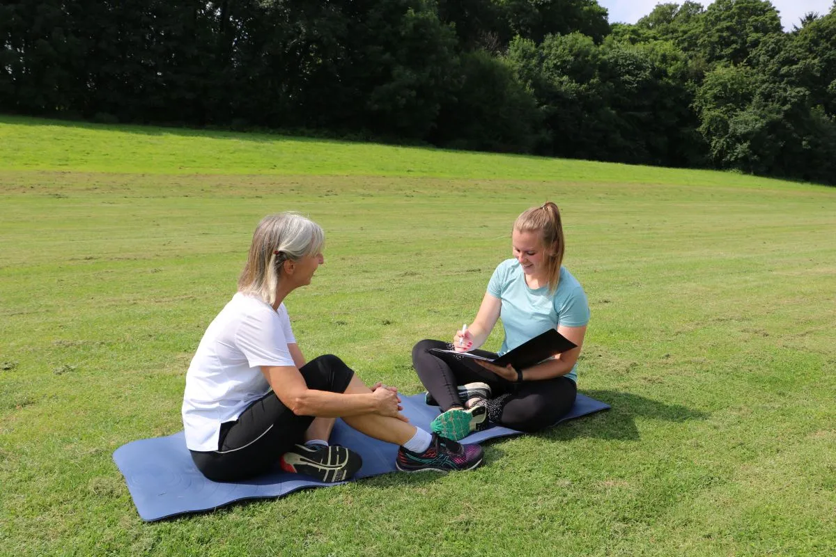 Julia Blum im Gespräch mit einer Kundin auf einer Trainingsmatte im Park